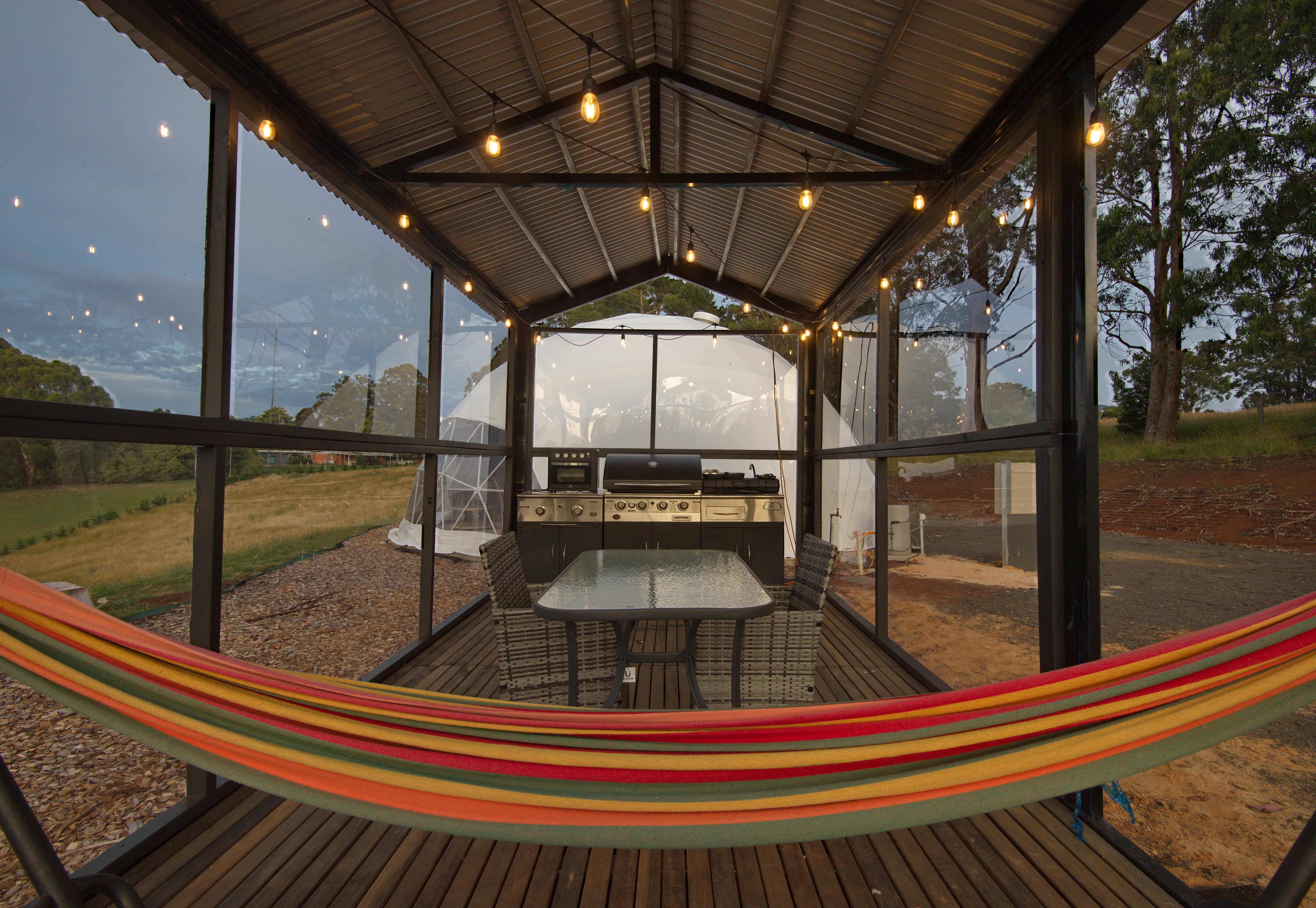 Covered outdoor BBQ kitchen with dining table and hammock at One Life Glamping Park