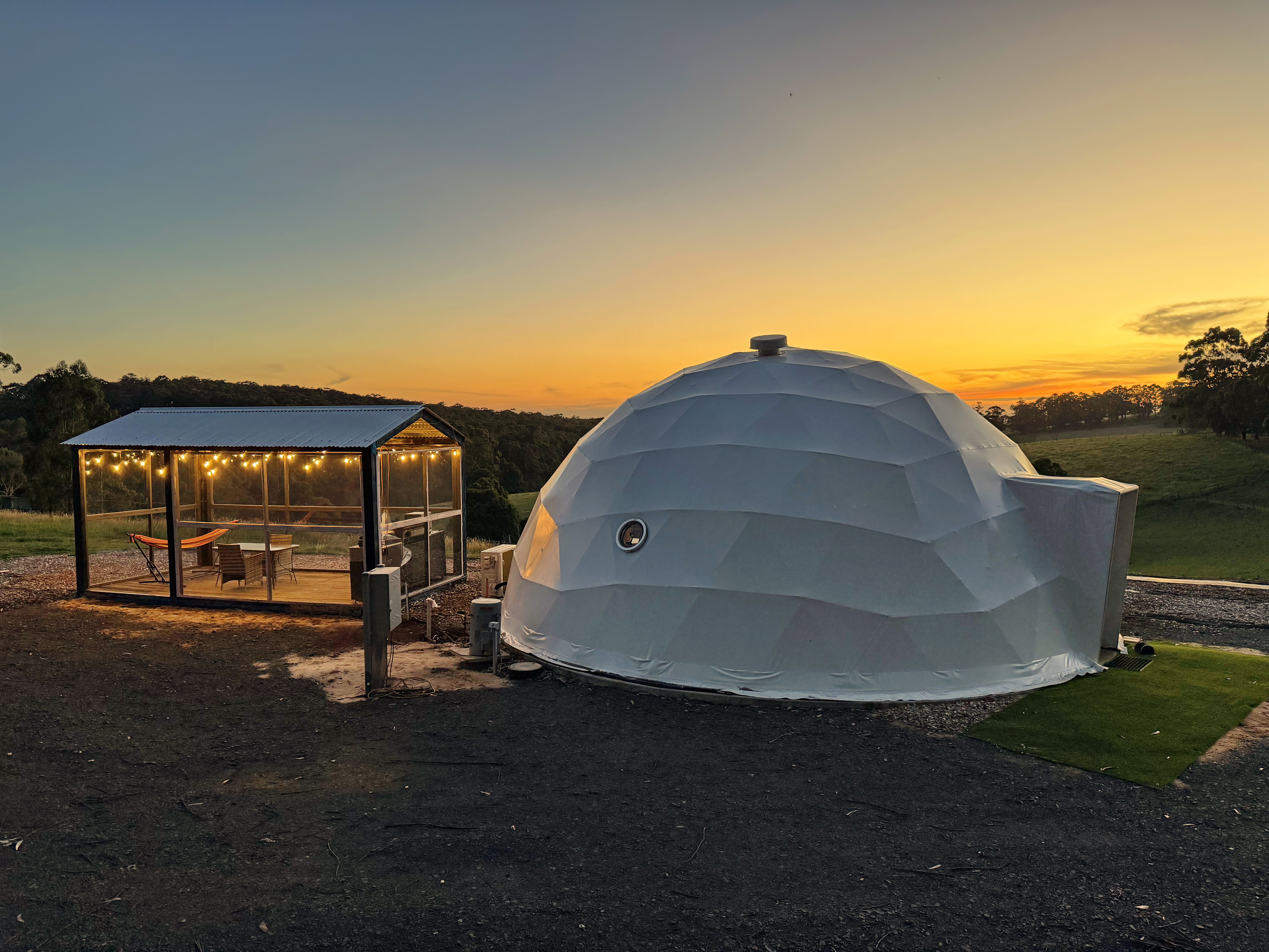 Side view of geodesic dome and lights at sunset overlooking Rawson hills